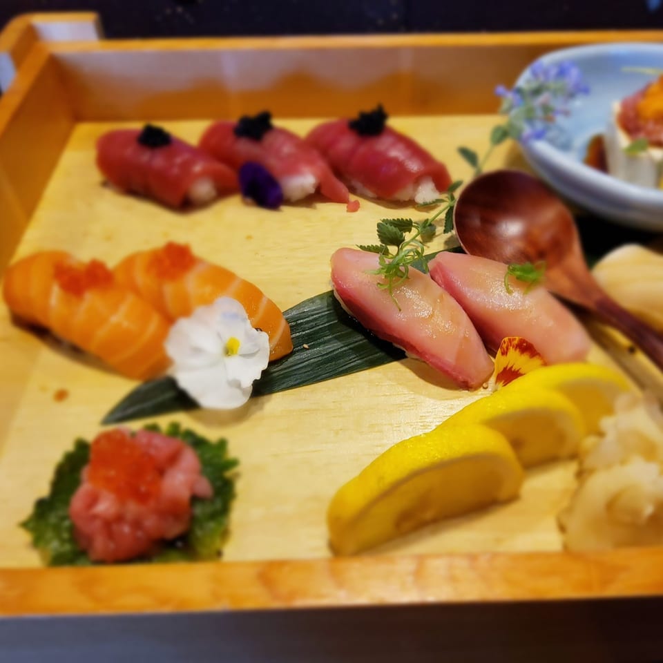 Assorted sushi and sashimi, including tuna, salmon, and yellowtail, artfully arranged on a wooden tray.