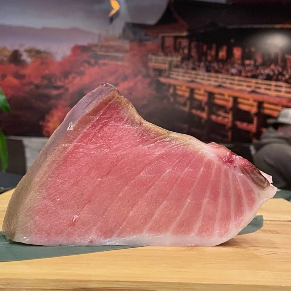 Large, fresh cut of pink tuna belly on a wooden board, ready for sushi preparation.